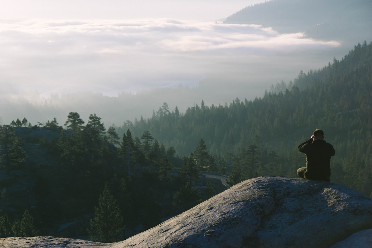 man sits on the mountain facing landscape view