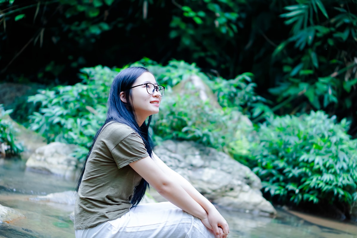 a woman with blue hair and glasses sitting on a rock