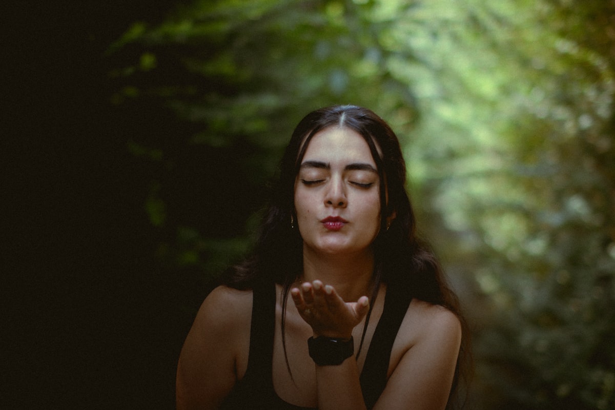 Woman blows a kiss with a forest backdrop.