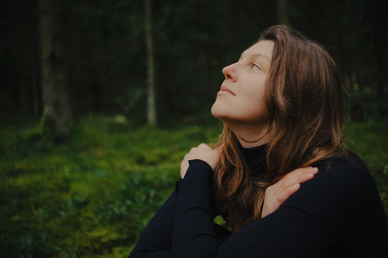 Woman with eyes closed embracing herself in forest