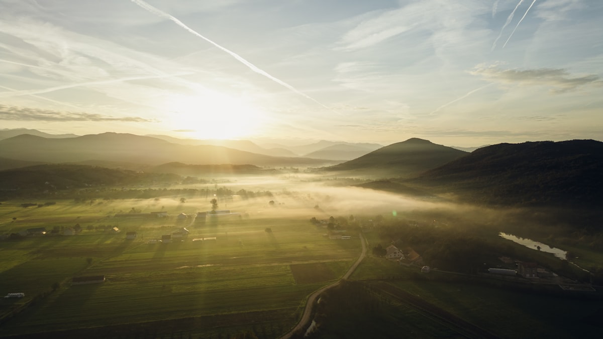 Sunlight streams over misty green valley and mountains.