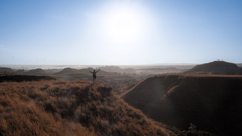 Person with arms raised on grassy hilltop at sunrise